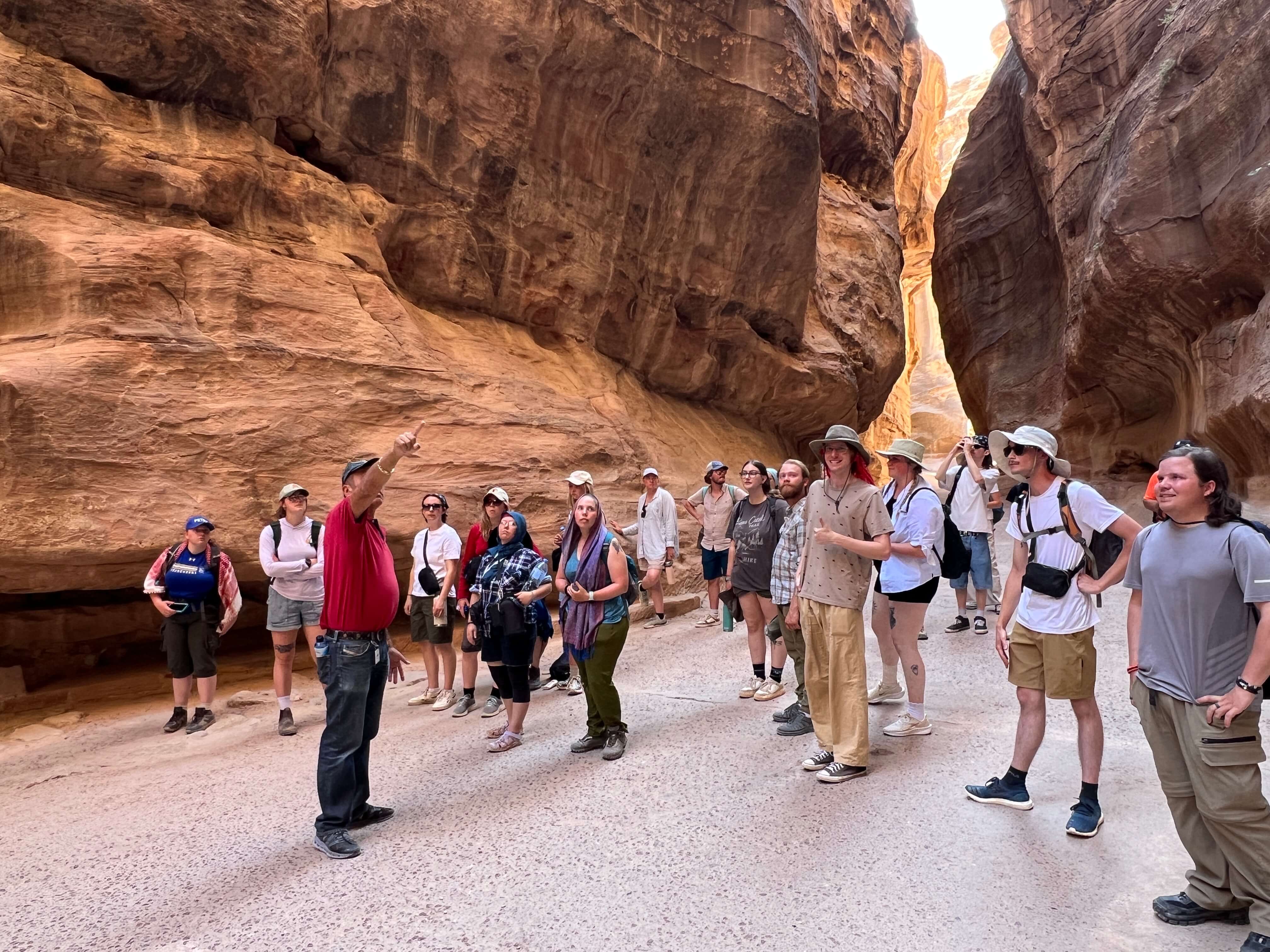 A group of students on a tour listening to a tour guide in a deep canyon.